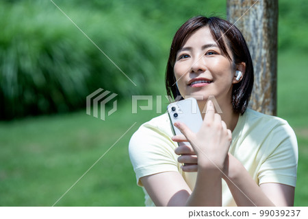 A woman listening to smartphone music in a fresh green park 99039237