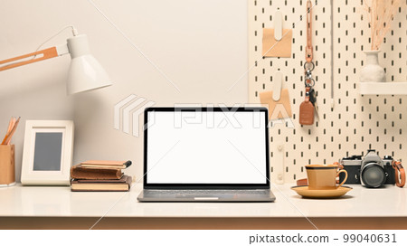 Comfortable workplace, laptop with blank screen, picture frame , camera and lamp on white table 99040631