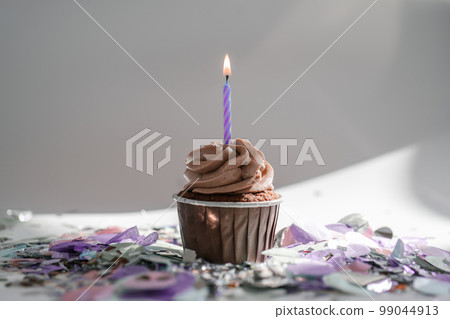 A cupcake with a candle stands on a white background with a shadow. A cupcake with a candle stands on a white background with a shadow. 99044913