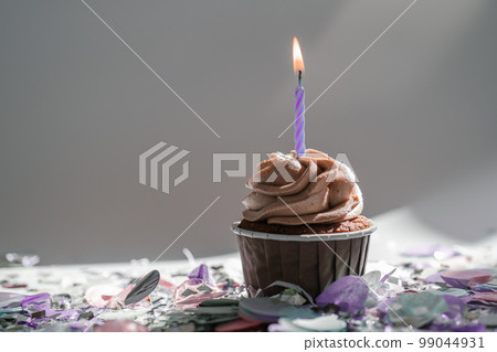 A cupcake with a candle stands on a white background with a shadow. A cupcake with a candle stands on a white background with a shadow. 99044931