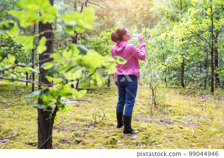 The girl drinks water in the forest on a summer sunny day. Survival in the forest, dehydration of the body. The girl drinks water in the forest on a summer sunny day. Survival in the forest, dehydration of the body. 99044946