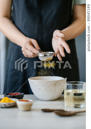 The girl sifts turmeric into a bowl. The girl sifts turmeric into a bowl. 99045149