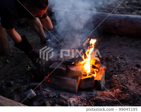A man throws firewood into a fire for cooking on a campfire in nature. Close-up 99045195