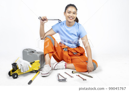 Asian woman car technician in uniform sitting with a car jack and toolkit box and wrench Asian woman car technician in uniform sitting with a car jack and toolkit box and wrench 99045767