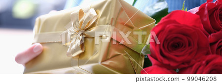 Bouquet of red roses and golden gift box in female hands 99046208