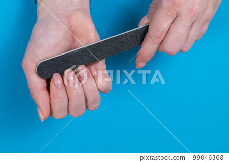 Woman filing her nails on a blue background. Woman filing her nails on a blue background. 99046368