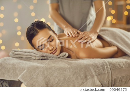 Relaxed beautiful young woman is enjoying professional body massage at a spa salon Relaxed beautiful young woman is enjoying professional body massage at a spa salon 99046373