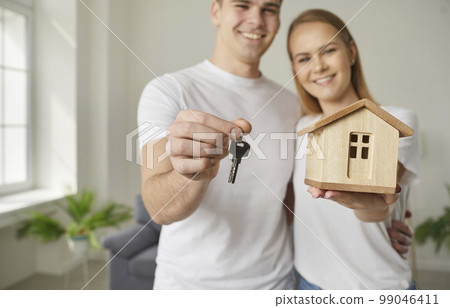Small house and key in hands of joyful couple who are happy about successful purchase of real estate 99046411