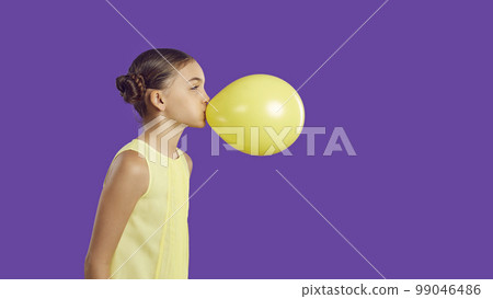 Cheerful funny little girl inflates yellow balloon isolated on vivid purple background. Cheerful funny little girl inflates yellow balloon isolated on vivid purple background. 99046486
