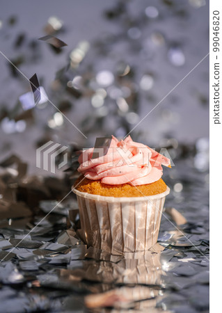 A cupcake with a pink cap stands among the flying silver confetti. A cupcake with a pink cap stands among the flying silver confetti. 99046820