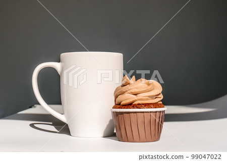 A cupcake or muffin stands next to a cup of coffee. A cupcake or muffin stands next to a cup of coffee. 99047022