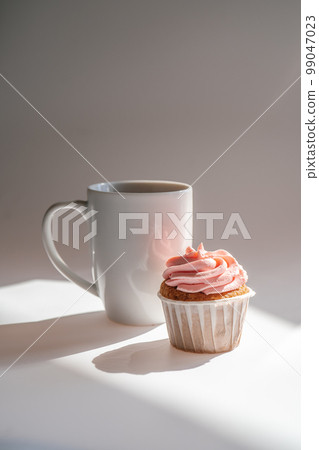 A cupcake or muffin stands next to a cup of coffee. A cupcake or muffin stands next to a cup of coffee. 99047023