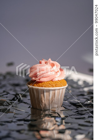 A cupcake with a pink cap stands among the flying silver confetti. 99047024