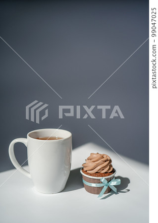 A cupcake or muffin stands next to a cup of coffee. A cupcake or muffin stands next to a cup of coffee. 99047025