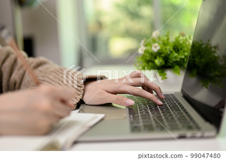 Side view close-up image of a woman in cozy sweater using laptop, typing on keyboard 99047480