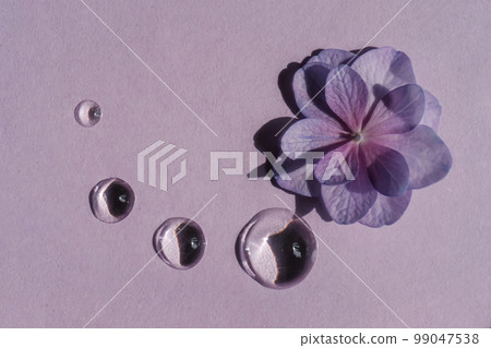 A drop of transparent cosmetic gel with flowers on a purple background. 99047538