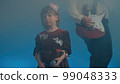 Little girl on stage in vintage dress, she sings into microphone and dances, her father plays an electric guitar. Color music is shining and smoke is billowing. Family time, creativity and hobbies 99048333