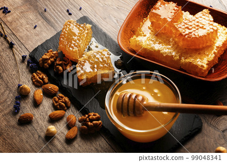 Honeycomb on slate tray with honey and nuts on kitchen table 99048341