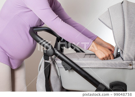 Mother chooses a stroller for her future baby in the store. Modern European comfortable strollers transformers 3 in 1 for kids. 99048738