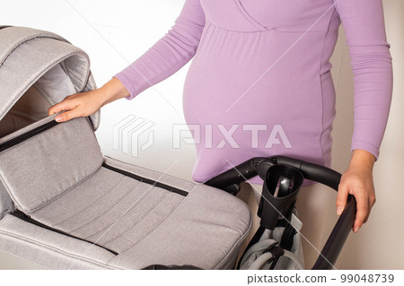 Mother chooses a stroller for her future baby in the store. Modern European comfortable strollers transformers 3 in 1 for kids. Mother chooses a stroller for her future baby in the store. Modern European comfortable strollers transformers 3 in 1 for kids. 99048739