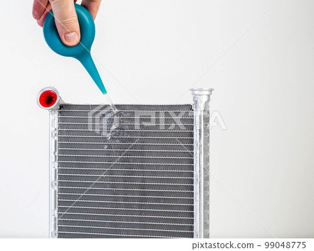 A jet of water from a syringe pours onto a car radiator. The concept of cleaning and flushing car radiators from pollution. Clogged radiator cells. Copy space for text 99048775