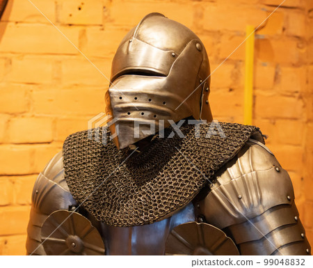 A warrior in metal armor and a helmet against a brick wall. Ancient outfit protection for warriors, legguards 99048832