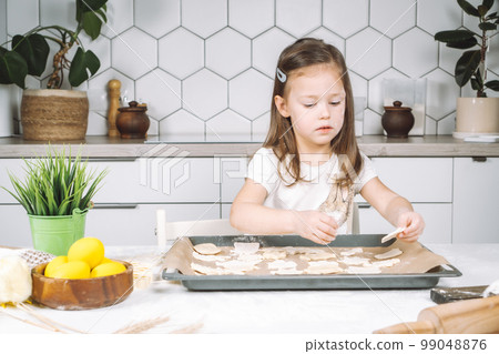 Portrait of little studiously kid girl, sitting chair kitchen, making different easter shape dough cookies, dripping pan 99048876
