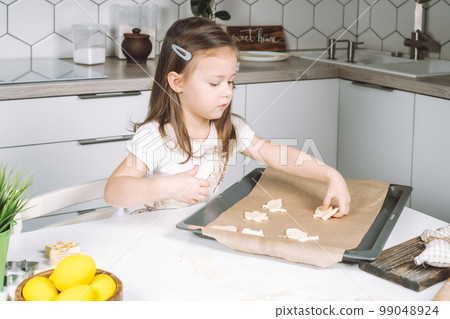Portrait of little studiously kid girl, sitting chair kitchen, making different easter shape dough cookies, dripping pan 99048924