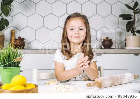 Portrait little smiling girl chef, sitting assistance, peparing, kneading dough, rolling pin flour, making shape cookies Portrait little smiling girl chef, sitting assistance, peparing, kneading dough, rolling pin flour, making shape cookies 99048930