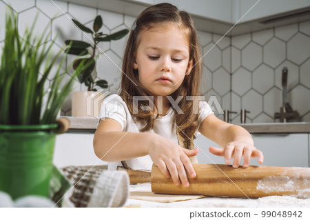 Portrait little studiously girl, learning rolling dough, making shape easter pastry. Holding rolling pin flour. Closeup 99048942