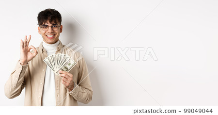 Handsome modern man in glasses showing dollar bills and okay gesture, making money, standing with cash on white background Handsome modern man in glasses showing dollar bills and okay gesture, making money, standing with cash on white background 99049044