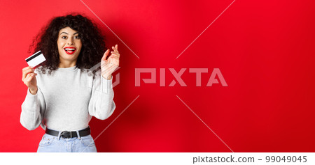 Excited woman telling about special deal, showing plastic card and looking happy, going shopping, standing on red background Excited woman telling about special deal, showing plastic card and looking happy, going shopping, standing on red background 99049045