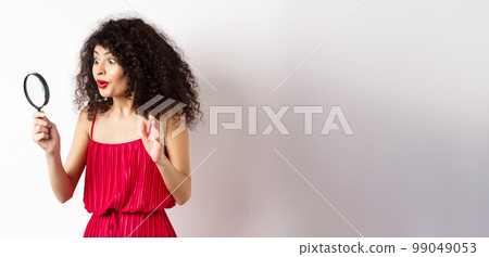Excited woman in red dress look through magnifying glass and smiling, found interesting promo, standing on white background Excited woman in red dress look through magnifying glass and smiling, found interesting promo, standing on white background 99049053