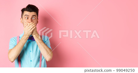 Funny young man covering mouth with hands and squint eyes, making clown grimaces, standing silly on pink background, entertain people Funny young man covering mouth with hands and squint eyes, making clown grimaces, standing silly on pink background, entertain people 99049250