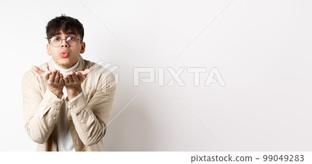 Cute boyfriend sending air kiss at camera on happy Valentines day, looking tender at lover, standing in casual clothes and glasses on white background Cute boyfriend sending air kiss at camera on happy Valentines day, looking tender at lover, standing in casual clothes and glasses on white background 99049283