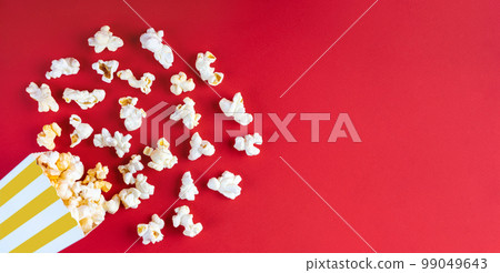 Tasty cheese popcorn falling out of a yellow striped carton bucket, isolated on red background Tasty cheese popcorn falling out of a yellow striped carton bucket, isolated on red background 99049643