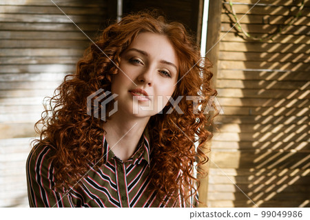 Portrait of happy redhead young woman near window Portrait of happy redhead young woman near window 99049986