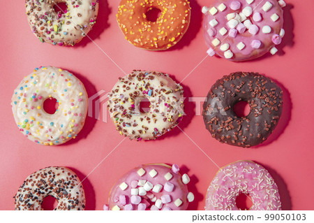 Donuts with icing on pastel pink background. Sweet donuts. top view assorted with various chocolate glazed and sprinkles, sugar sweets concept 99050103