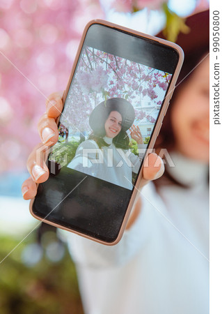 woman shooting her self on the phone under blooming sakura tree 99050800