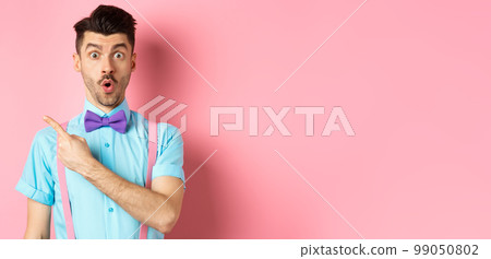 Check it out. Amazed caucasian man with moustache, wearing bow-tie, saying wow and pointing left, showing advertisement, standing on pink background 99050802