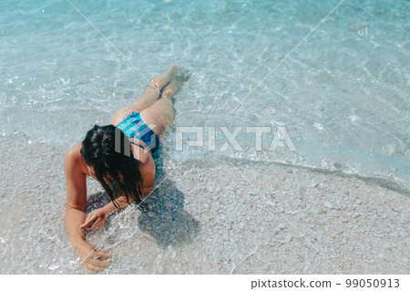 beautiful woman in blue swimsuit laying down in sea water at the beach 99050913