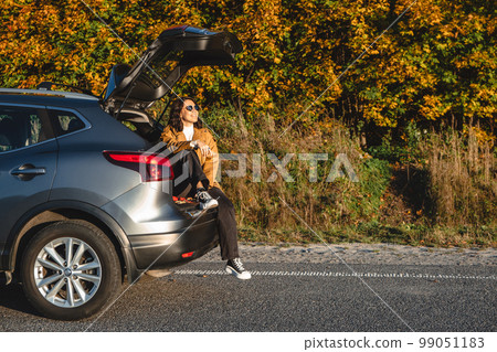 As she sits in the trunk of her vehicle, a woman enjoys the sun as she enjoys the warmth 99051183