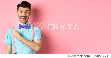 Happy young man checking out promo offer, smiling amazed and pointing finger left at copy space, standing near logo on pink background 99051271