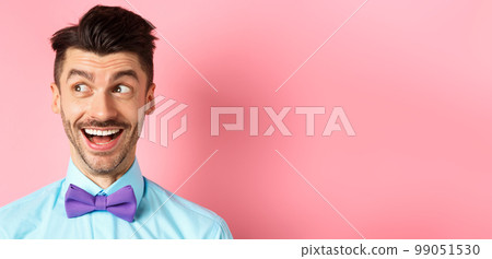 Close up of cheerful smiling guy, looking aside at logo with happy face, checking out cool promo offer, standing against pink background Close up of cheerful smiling guy, looking aside at logo with happy face, checking out cool promo offer, standing against pink background 99051530