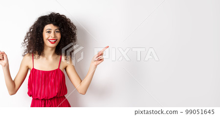 Happy lady with curly hairstyle and red lips, smiling white teeth, pointing sideways at two ways, showing advertisements aside, standing on white background 99051645