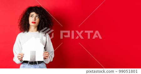 Real estate. Sad woman dreaming of buying apartment, holding paper house cutout and looking up distressed, standing on red background Real estate. Sad woman dreaming of buying apartment, holding paper house cutout and looking up distressed, standing on red background 99051801