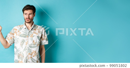 Displeased tourist in hawaiian shirt, looking and pointing left disappointed, complaining something bad, standing on blue background Displeased tourist in hawaiian shirt, looking and pointing left disappointed, complaining something bad, standing on blue background 99051802