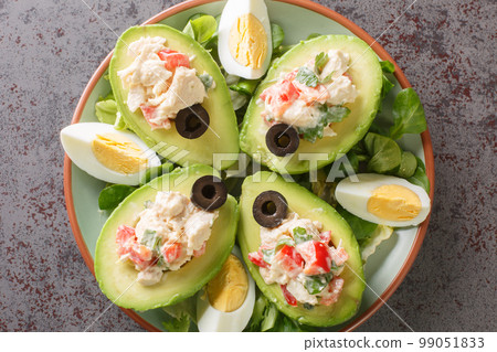 Avocado halves stuffed with chicken salad close-up on a plate. Horizontal top view 99051833