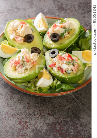 Fresh avocado stuffed with chicken salad on a bed of leafy greens close-up on a plate. Vertical Fresh avocado stuffed with chicken salad on a bed of leafy greens close-up on a plate. Vertical 99051842