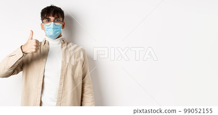 Covid-19, health and real people concept. Satisfied guy in sterile face mask and glasses, showing thumb up in approval, give positive feedback, standing on white background 99052155